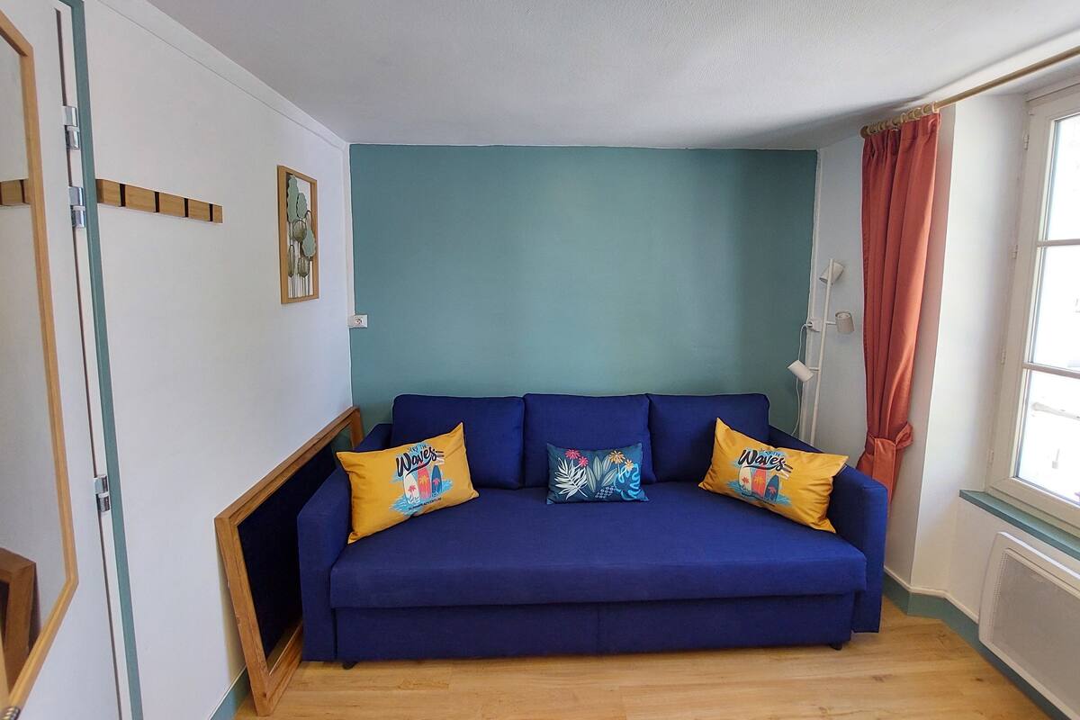A room with a blue sofa, two yellow pillows, a framed picture, and a window with a curtain.