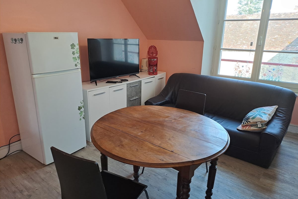 A compact living space with a kitchenette, a flat-screen TV, a dining table, a sofa, and a window with a view of the outside.