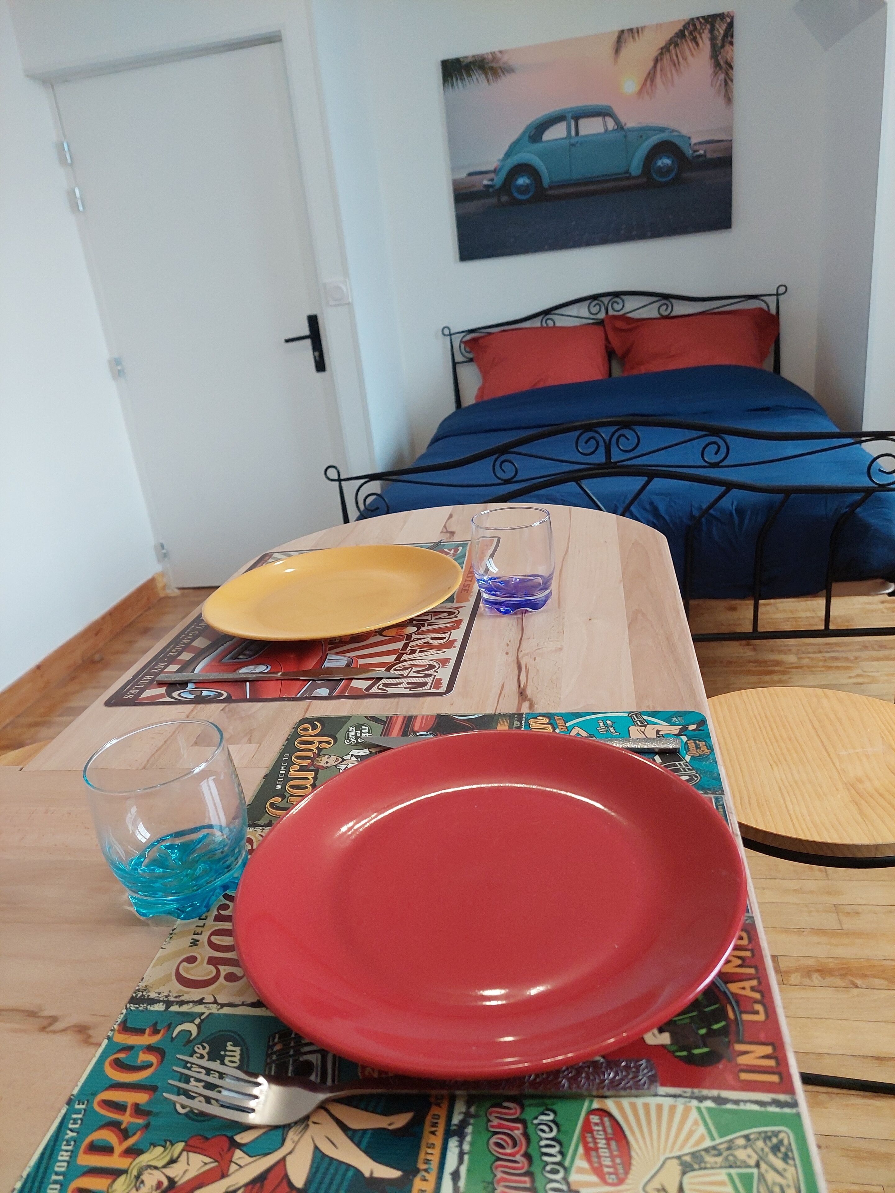 Een eettafel met een rood bord, een geel bord en een glas met blauwe vloeistof. De tafel heeft een placemat met een vintage automotief thema.