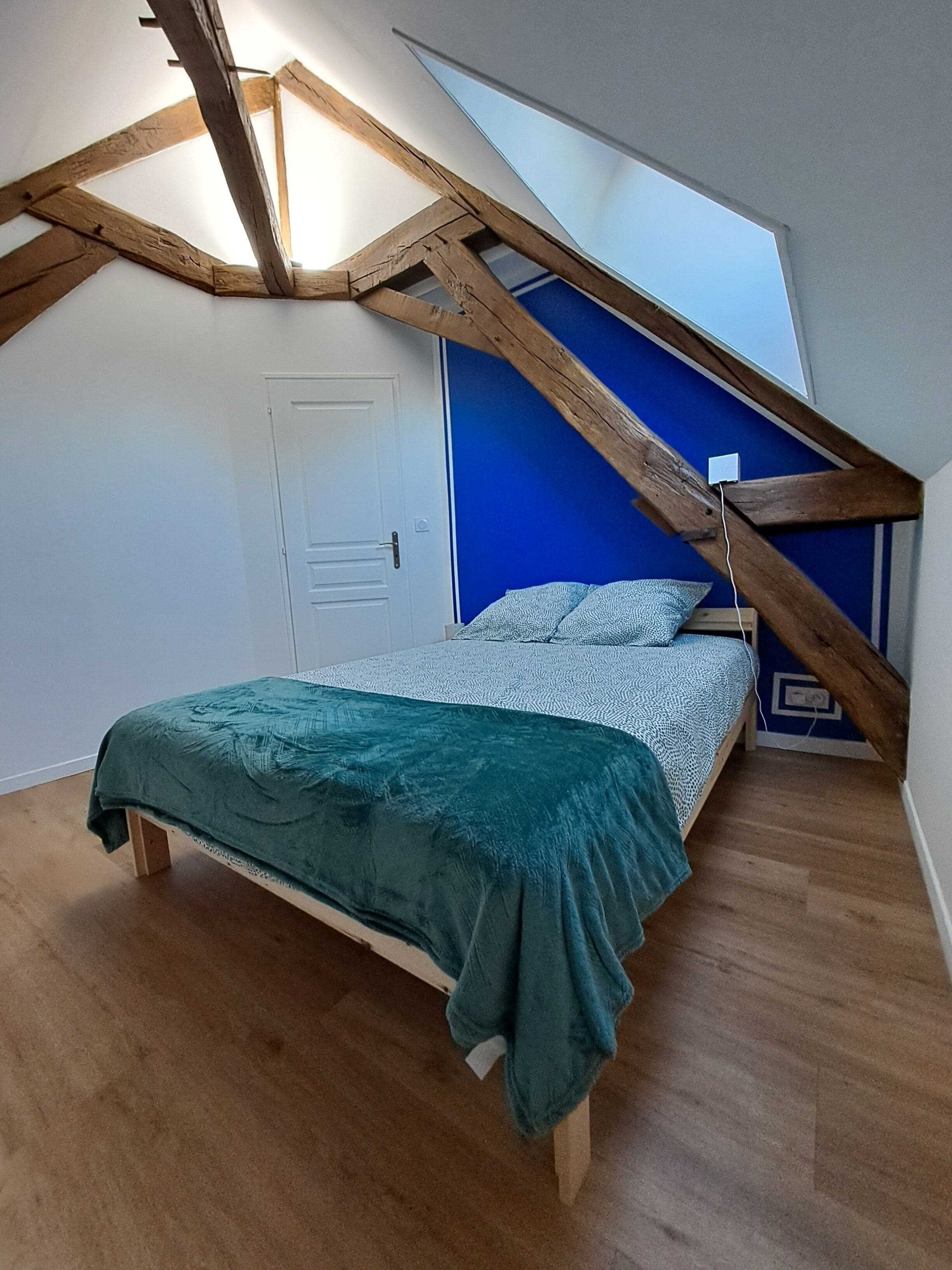 Ein Schlafzimmer mit geneigter Decke, einem Bett mit türkisfarbenem Überwurf und einer blauen Akzentwand.