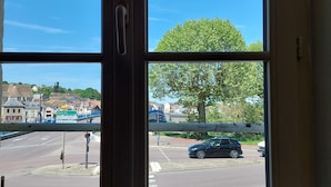 A window with a view of a road, a tree, and some buildings. - Le km99 (Pont-sur-Yonne)