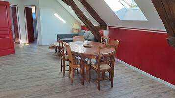 A dining area with a round table and six chairs, wooden beams on the ceiling, and a skylight.