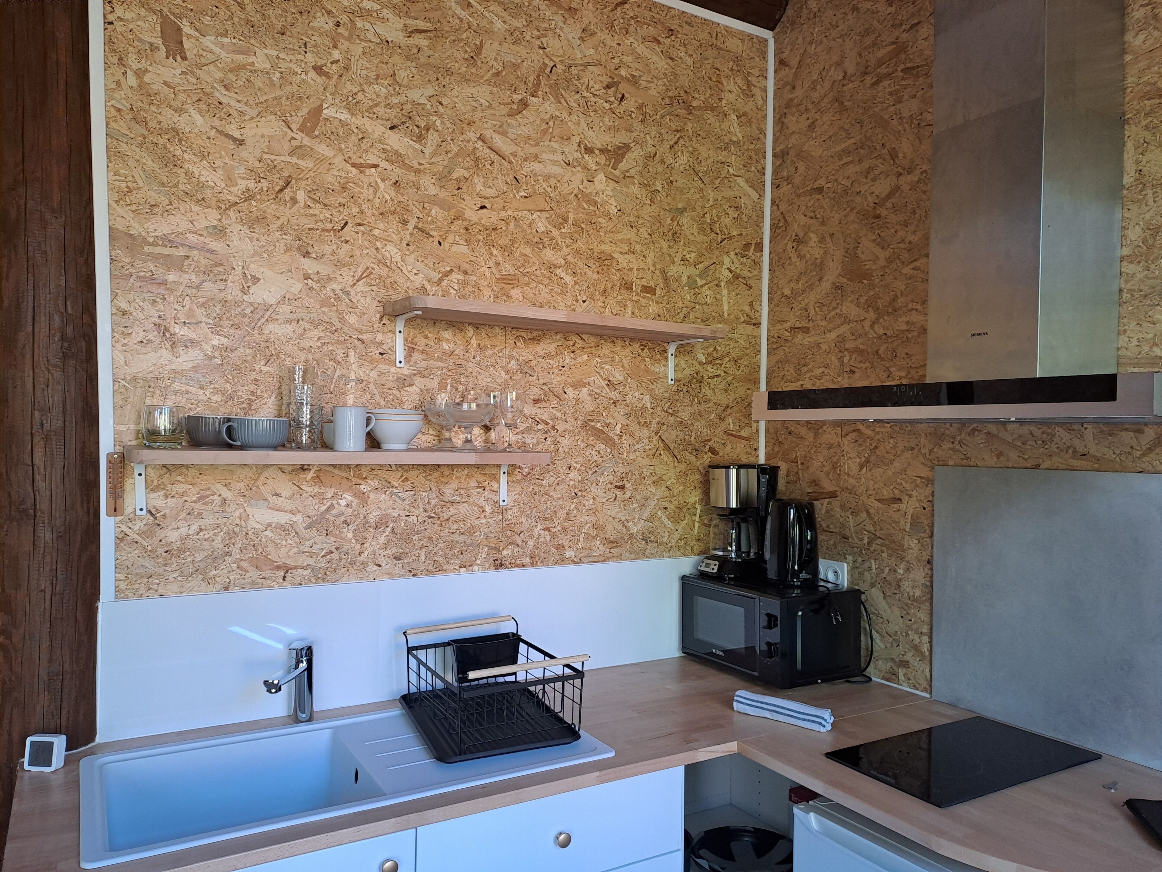 A kitchen with a wooden backsplash, a built-in microwave, a coffee maker, and a sink with a dish rack.
