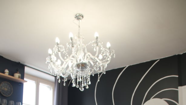 A modern living room with a dark-colored sofa, a glass coffee table, and a chandelier. - Le km99 (Pont-sur-Yonne)