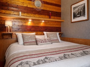 Un lit avec une couvre-lit à motifs de montagne, une tête de lit en bois et des lampes de chevet.