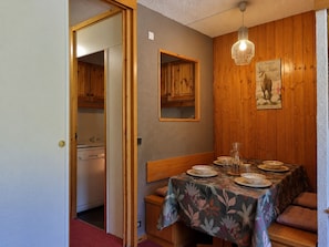 Un coin repas avec une table dressée pour quatre personnes, des lambris en bois sur les murs et un luminaire suspendu.
