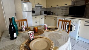 Une table à manger dressée avec des assiettes, des couverts et des tasses, un lave-linge et un téléviseur dans un coin cuisine.
