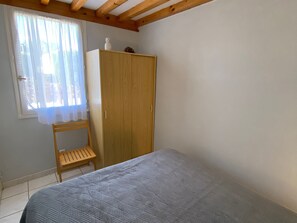 Une chambre à coucher avec un lit, une armoire en bois, une petite chaise en bois et une fenêtre ornée de rideaux légers.