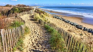 Un sentier de sable bordé d’une clôture en bois, qui mène à l’océan.