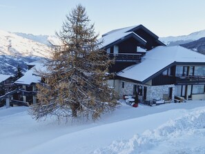 Un chalet de dos pisos con fachada de piedra, balcones de madera y un techo cubierto de nieve.