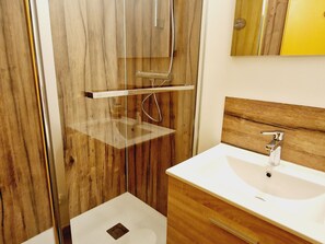 Une salle de bain avec un meuble-lavabo en bois, un lavabo blanc et une cabine de douche en verre.