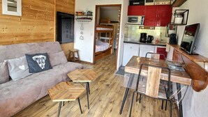 A compact living space with a sofa, a dining table, a kitchen area, and a bunk bed. - Cozy Studio Near Ski Slopes, Ideal for Families, Fully Equipped Kitchen (La Plagne Montalbert)