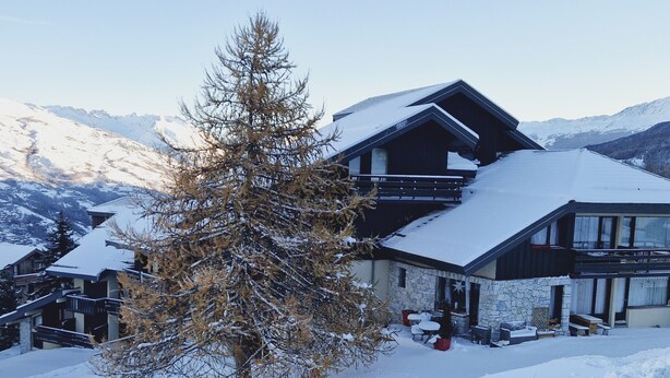 A two-story chalet with a stone facade, wooden balconies, and a snow-covered roof. - Cozy Studio Near Ski Slopes, Ideal for Families, Fully Equipped Kitchen (La Plagne Montalbert)