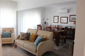 A living room with a beige sofa, a wooden dining table, and a chair. - Arruda Luxury Apartment With AC (Cascais)