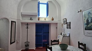 Une pièce avec une porte bleue, une petite fenêtre, une table sur laquelle se trouve un bol, et une chaise.