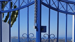 Une porte en métal bleue, d’où l’on aperçoit la mer et, au loin, des bâtiments blancs.