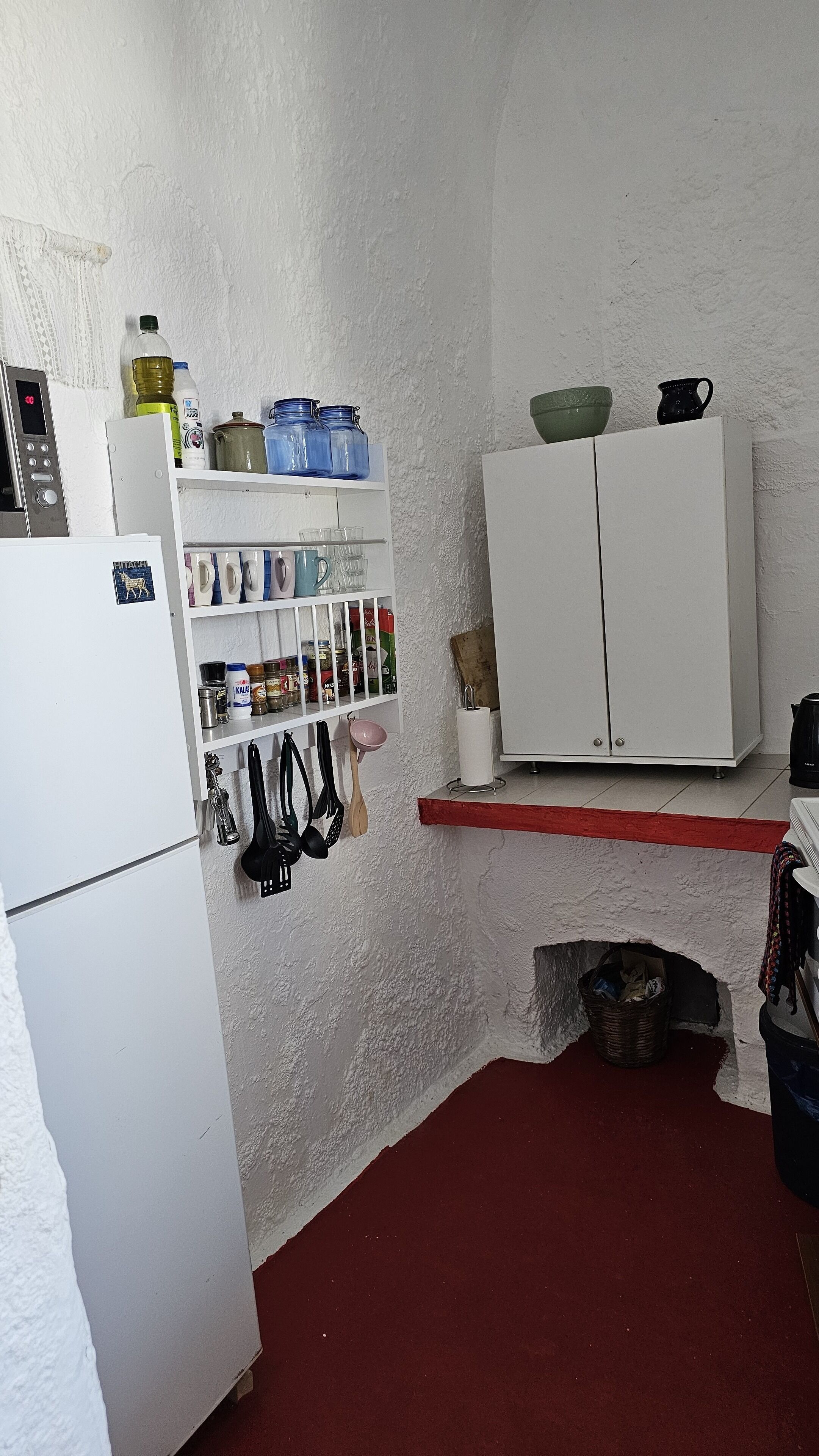 A compact kitchen with white cabinets, a refrigerator, and various kitchen utensils and containers.