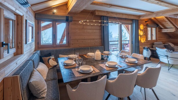 A cozy wooden dining area with a high ceiling and exposed beams, large windows, and a view of the outdoors. - Luxury chalet Alpe d'Huez with spa and ski-in/ski-out (Huez)