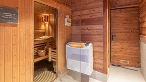 A wooden sauna room with a bench, a wooden bucket, and a sauna heater. - Luxury chalet Alpe d'Huez with spa and ski-in/ski-out (Huez)