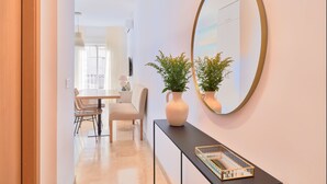 Un intérieur moderne comprenant un coin repas, une console agrémentée d’un vase et d’un miroir, et un couloir menant à une autre pièce.