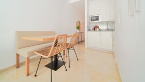 Une cuisine moderne avec des meubles blancs, un four à micro-ondes et un banc en bois agrémenté de chaises en osier.