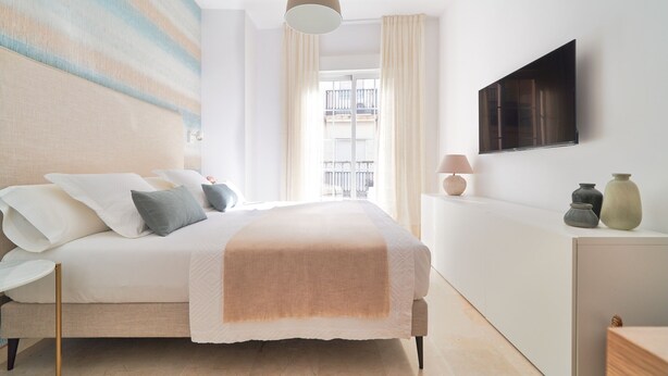 Une chambre à coucher moderne, équipée d’un lit, d’une table de chevet, d’une lampe et d’un téléviseur à écran plat fixé au mur.
