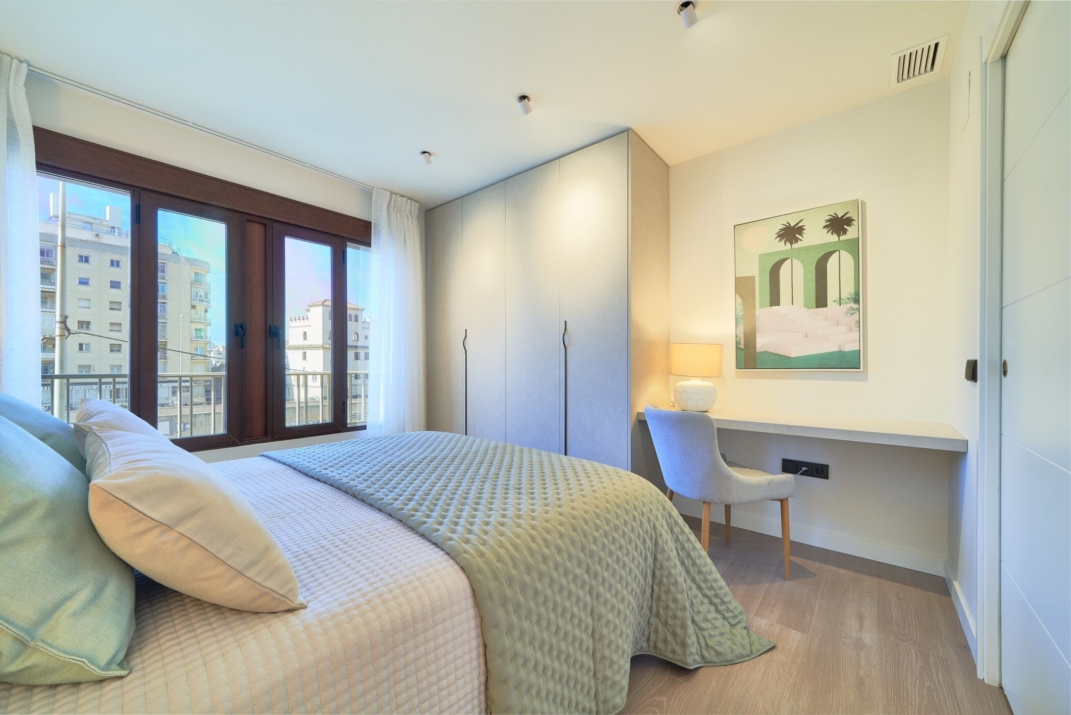Quarto com cama, escrivaninha, cadeira, janela e um quadro na parede.