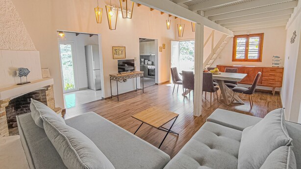 A spacious living area with a fireplace, a dining table with chairs, and a kitchen in the background.