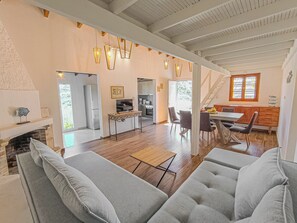 A spacious living area with a fireplace, a dining table with chairs, and a kitchen in the background. - Beach Walk Haven: Cozy Home 8 Minutes from Almyrida Beach (Almyrida)