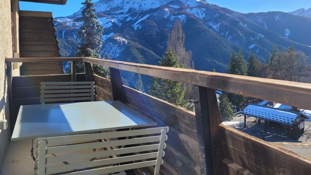 A balcony with a table and chairs, overlooking a mountain range with snow-capped peaks. - Luxury 8-Person Apartment, South Balcony, 120m from Pra-Loup 1500 Lift (Pra-Loup)