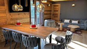 A modern interior with a wooden dining table, grey upholstered chairs, a sofa, and pendant lighting. - Luxury 8-Person Apartment, South Balcony, 120m from Pra-Loup 1500 Lift (Pra-Loup)