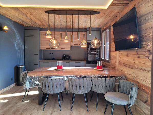 Eine moderne Küche mit Holzelementen, Pendelleuchten, einer großen Kochinsel und einem an der Wand befestigten Flachbildfernseher.