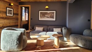 A cozy living room with a sofa, armchairs, a coffee table, and a wooden accent piece. - Luxury 8-Person Apartment, South Balcony, 120m from Pra-Loup 1500 Lift (Pra-Loup)