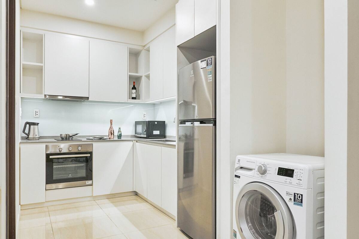 Une cuisine moderne avec des armoires blanches, des appareils en acier inoxydable et un lave-linge encastré.