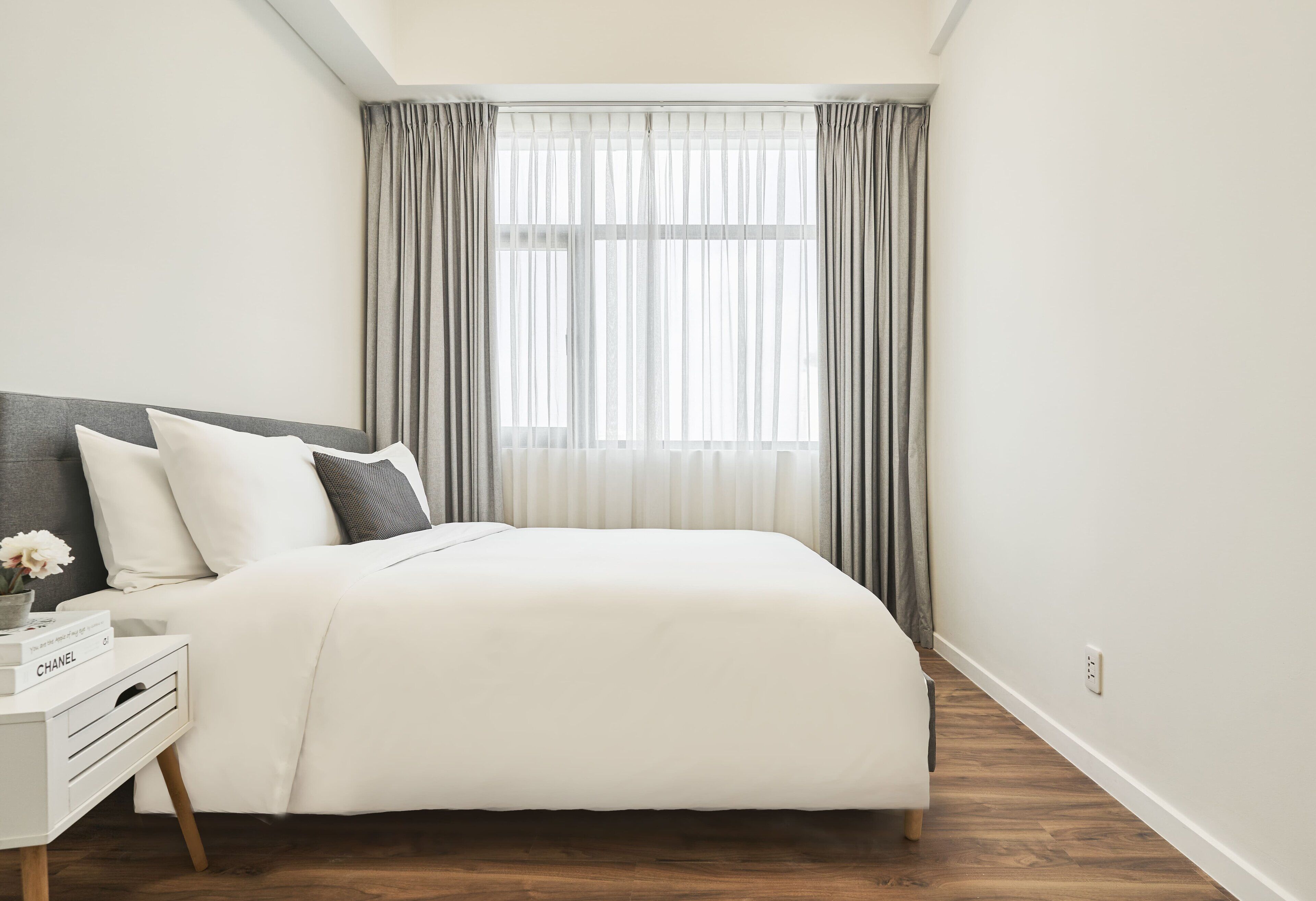 Un dormitorio moderno con una cama grande, una mesita de noche con lámpara y una ventana con cortinas.