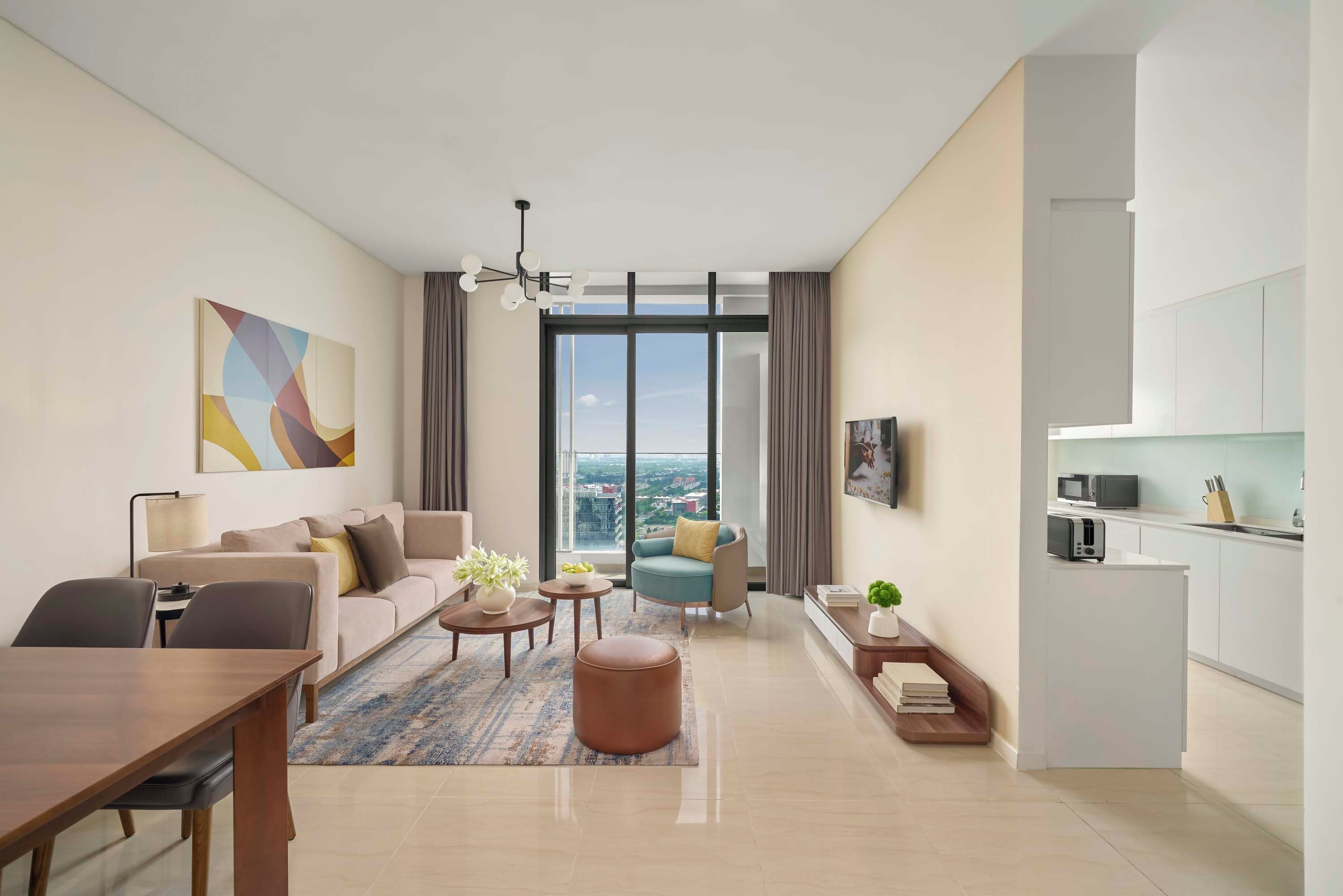 A modern living room with a sofa, coffee table, and chairs, a dining area with a table and chairs, a kitchen with a microwave and toaster, and a large window with a view.