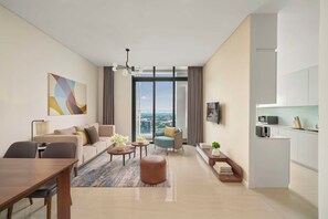 A modern living room with a sofa, coffee table, and chairs, a dining area with a table and chairs, a kitchen with a microwave and toaster, and a large window with a view. - RichLane Residences Managed by The Ascott Limited (Ho Chi Minh City)