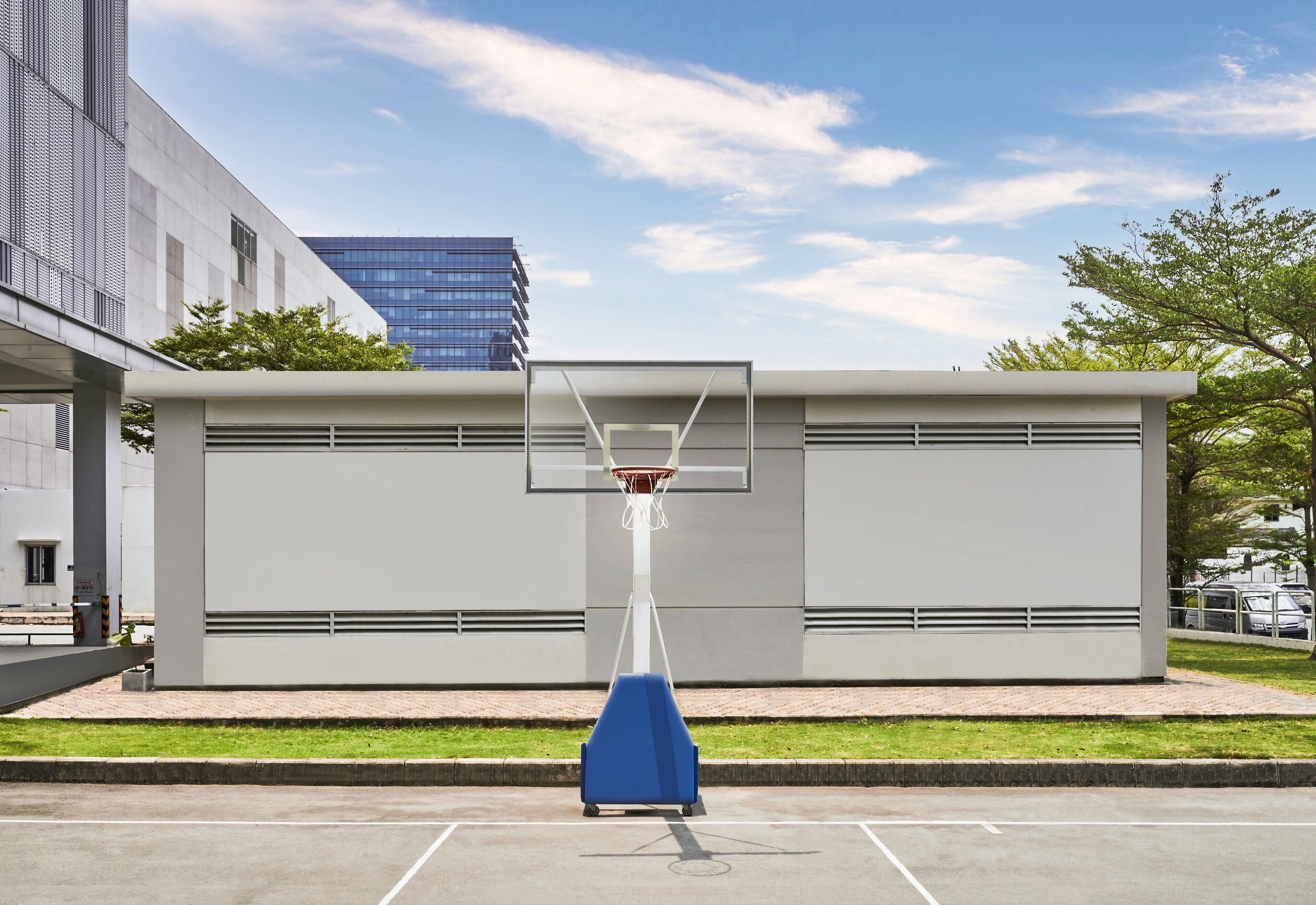 A basketball court with a hoop and a blue protective cover, located in front of a modern building with a glass facade.