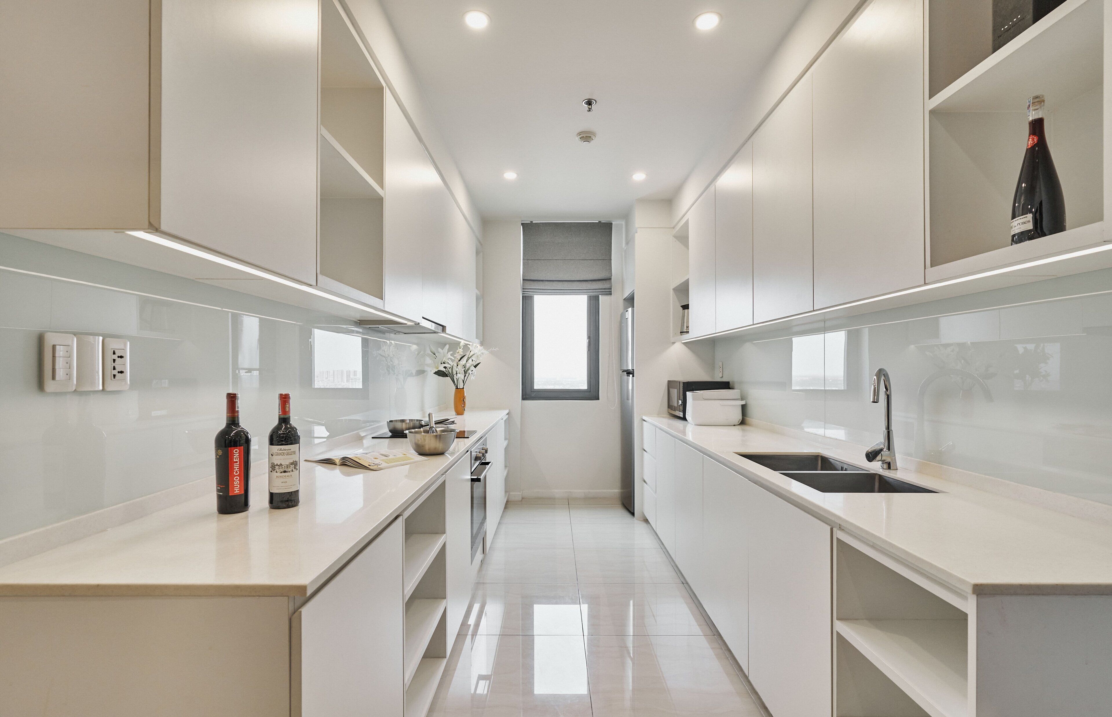 A modern kitchen with white cabinetry, a central island, and two wine bottles.