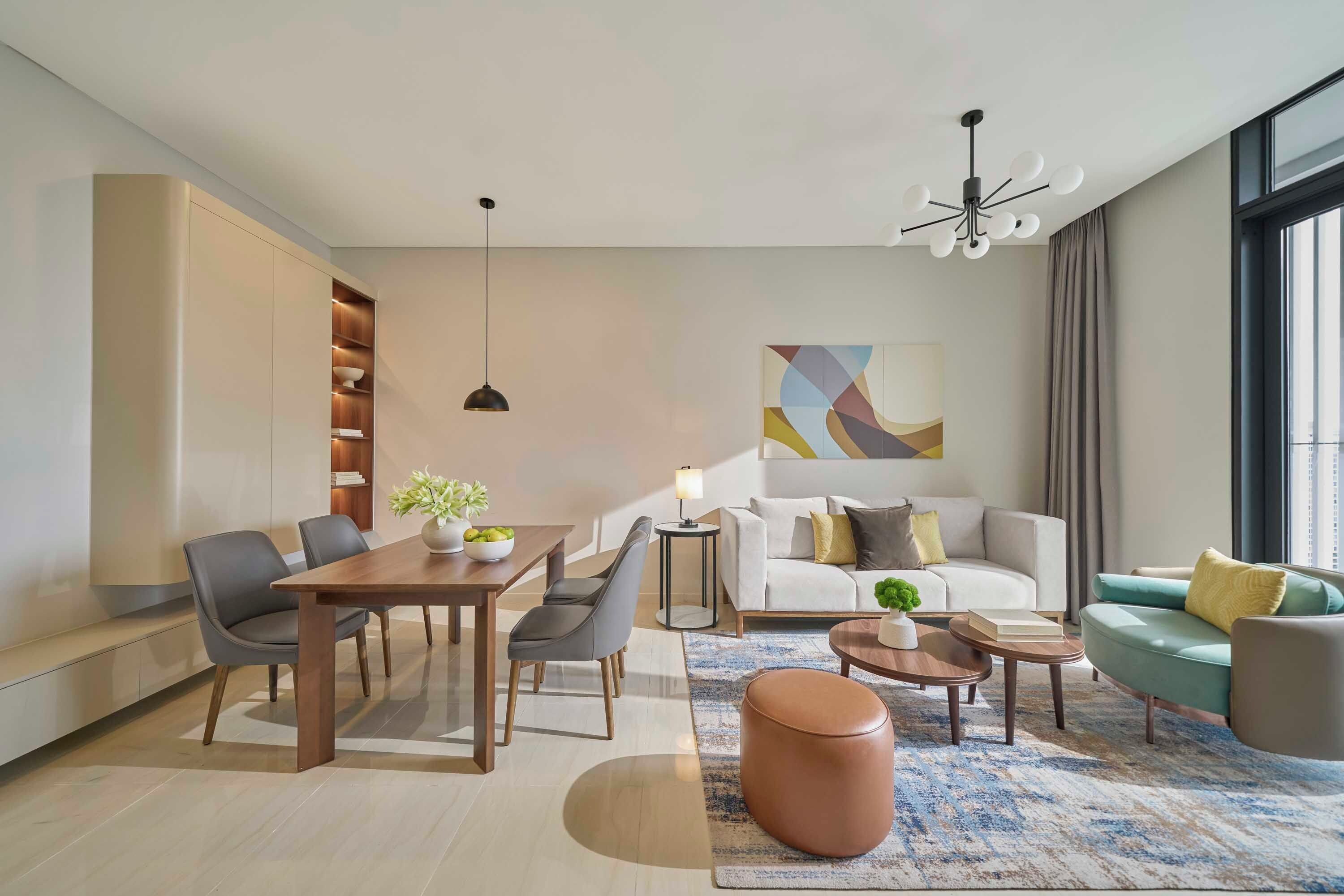 Un salon moderne comprenant un coin repas, un ensemble de canapés, une table basse et une grande fenêtre laissant entrer la lumière naturelle.