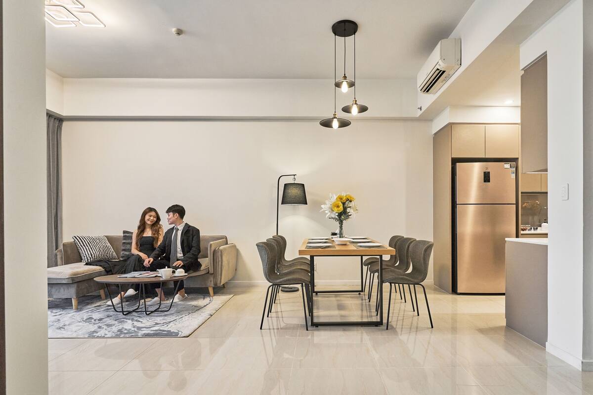 Un salon moderne comprenant un canapé, une table à manger et des chaises. Il y a également un coin cuisine avec un réfrigérateur et un appareil de climatisation.