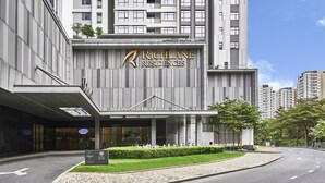 Un bâtiment moderne portant l’inscription « Richlane Residences », et un hall d’entrée bien entretenu avec une allée pavée et des espaces verts.