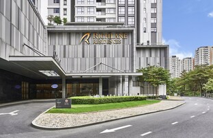 Un edificio moderno con el letrero "Richlane Residences" y un área de entrada bien cuidada, con entrada pavimentada y vegetación.