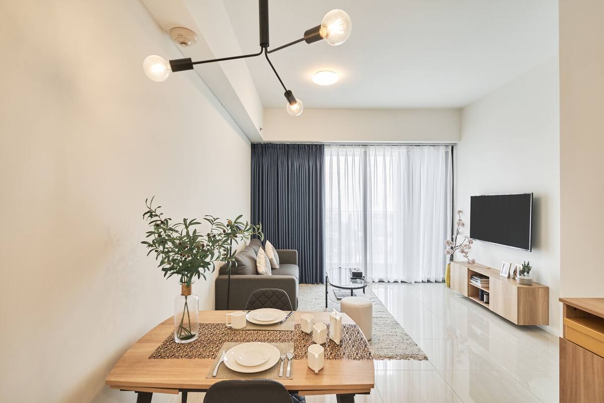 Un salon moderne comprenant un coin repas, un téléviseur à écran plat fixé au mur et une grande fenêtre avec des rideaux.