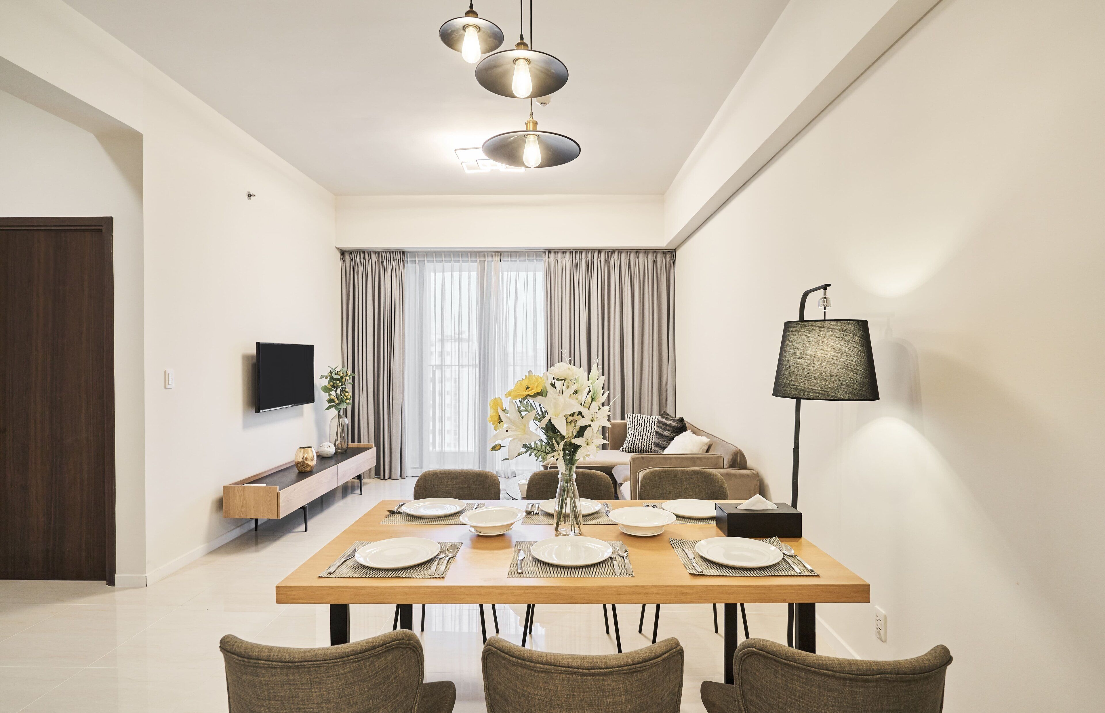 A modern dining room with a wooden table set for four, a sofa, and a TV on the wall.