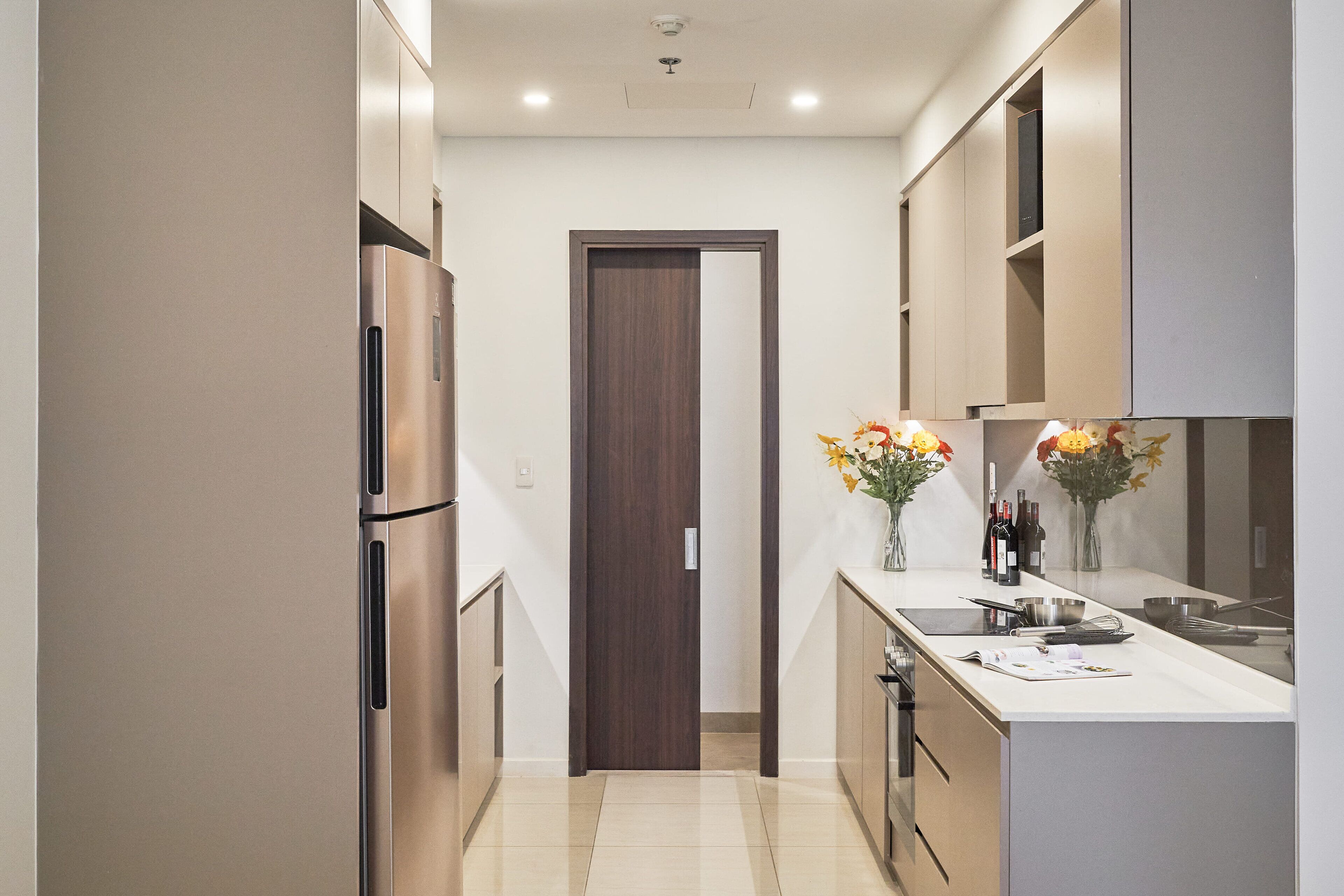 Una cucina moderna con frigorifero in acciaio inox, una porta in legno e un piano di lavoro bianco.