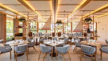 A spacious restaurant with multiple dining areas, wooden tables, and wicker chairs.