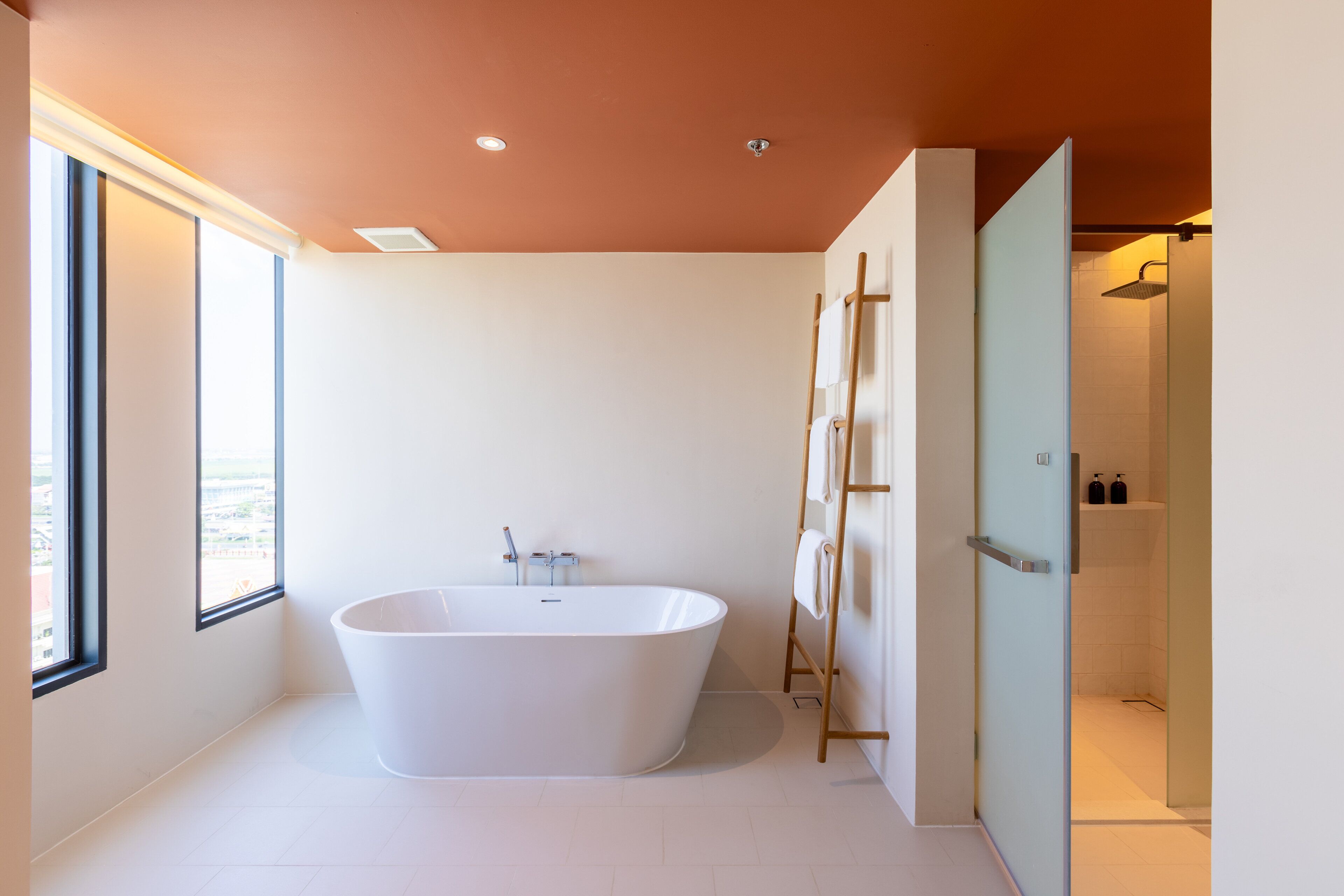 A modern bathroom with a freestanding bathtub, a glass shower enclosure, and a large window providing natural light.