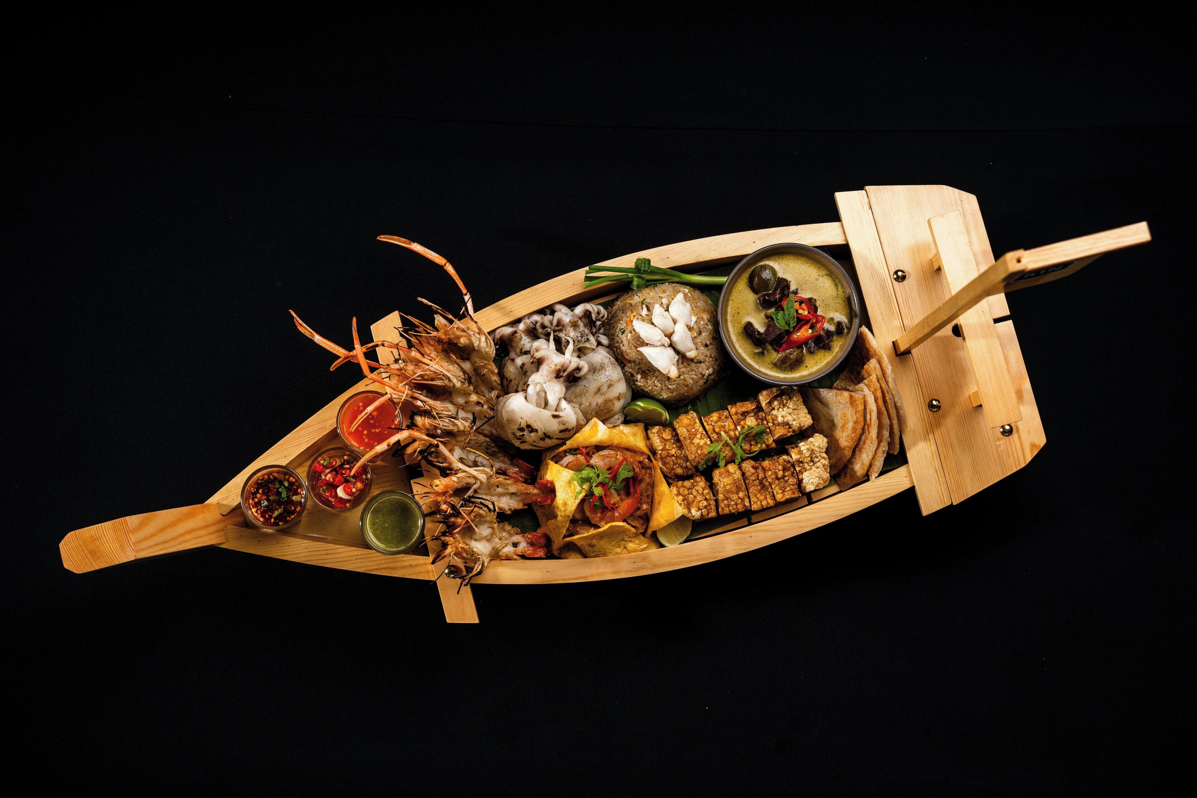 A wooden boat filled with various food items and condiments.