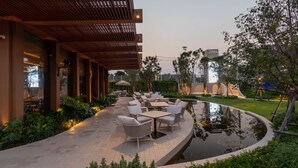 Un área de patio al aire libre con mobiliario, un pequeño estanque y una pérgola de madera.
